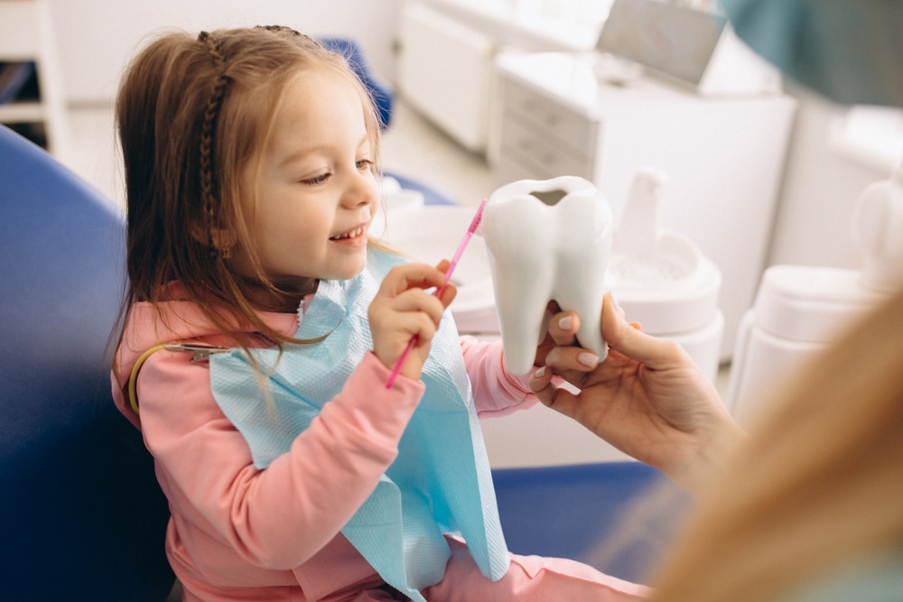 A child brushing a model of a tooth at a pediatric dentist’s office